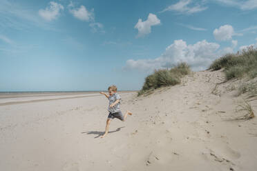 Glücklicher Junge läuft am Strand an einem sonnigen Tag - MFF09181