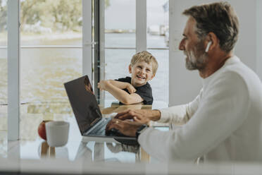 Glücklicher Junge sieht seinen Vater an, der am Laptop arbeitet - MFF09183