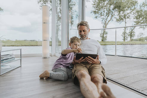 Smiling father with son using tablet PC sitting on floor - MFF09207