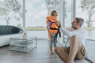 Father adjusting life jacket for son at home - MFF09211