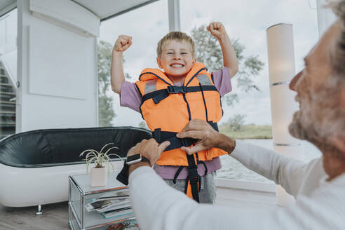 Glücklicher Sohn mit Schwimmweste beim Muskeltraining zu Hause - MFF09213