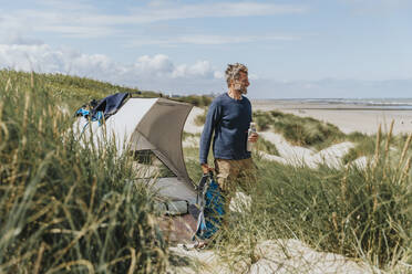 Glücklicher reifer Mann beim Zelten an einem sonnigen Tag am Strand - MFF09219