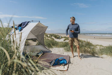 Happy man with smart phone standing at beach - MFF09222