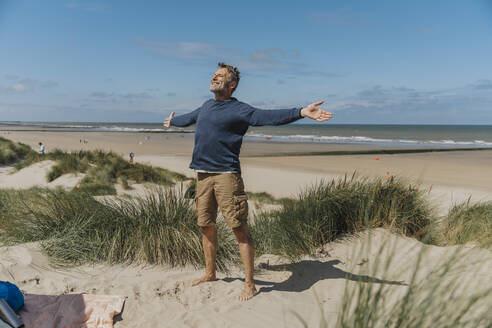 Happy mature man with arms outstretched standing at beach - MFF09225