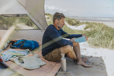 Mature man reading book at beach on sunny day - MFF09226