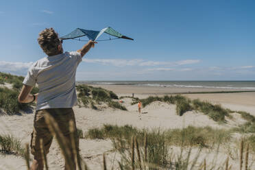 Älterer Mann lässt an einem sonnigen Tag am Strand einen Drachen steigen - MFF09229