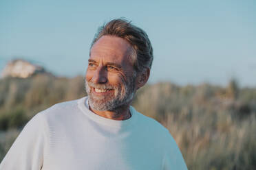 Happy mature man with beard looking away at beach - MFF09235