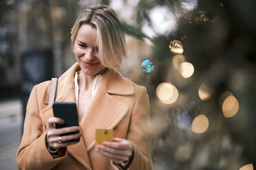 Lächelnde Frau, die eine Kreditkarte benutzt, um mit einem Smartphone zu bezahlen - AGOF00276