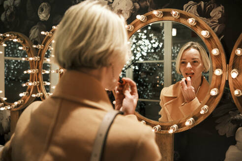 Beautiful woman applying lipstick looking in mirror - AGOF00284