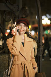 Lächelnde Frau mit Hut spricht nachts am Telefon - AGOF00289