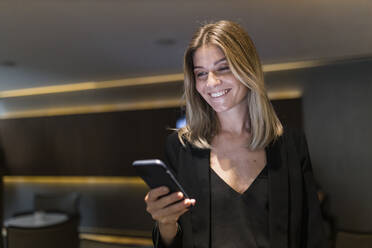 Lächelnde Geschäftsfrau mit Smartphone in der Lobby eines Hotels - JRVF03051