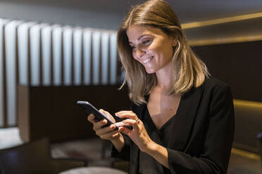 Glückliche Geschäftsfrau mit Smartphone in der Lobby eines Hotels - JRVF03052