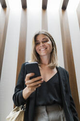 Happy businesswoman using smart phone in front of wall - JRVF03055