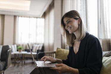 Lächelnde Geschäftsfrau mit Laptop auf dem Sofa in der Lobby eines Hotels - JRVF03059