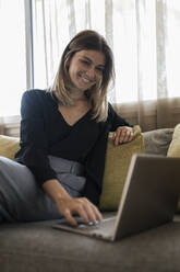 Glückliche Geschäftsfrau mit Laptop auf dem Sofa im Hotel - JRVF03060