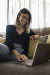 Happy businesswoman using laptop on sofa at hotel - JRVF03060