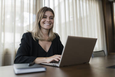 Smiling businesswoman using laptop on table at hotel - JRVF03083
