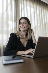 Lächelnde Geschäftsfrau sitzt mit Laptop auf dem Tisch - JRVF03084