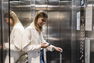 Smiling businesswoman using smart phone in elevator - JRVF03093