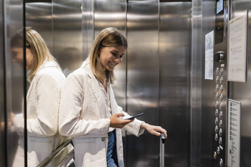 Lächelnde Geschäftsfrau mit Smartphone im Aufzug - JRVF03093