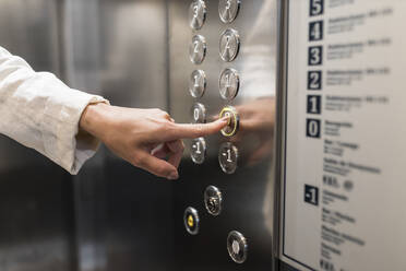 Die Hand einer Geschäftsfrau drückt die Aufzugstaste - JRVF03095