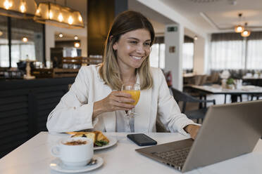 Lächelnde Geschäftsfrau mit Saftglas und Laptop im Restaurant - JRVF03105