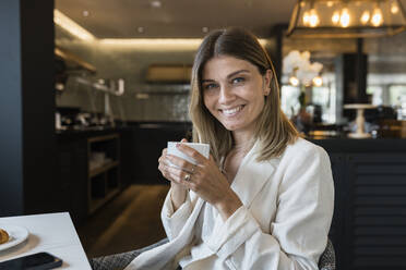 Smiling businesswoman holding coffee cup at restaurant - JRVF03107