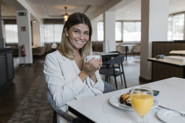 Happy businesswoman holding coffee cup at restaurant - JRVF03108