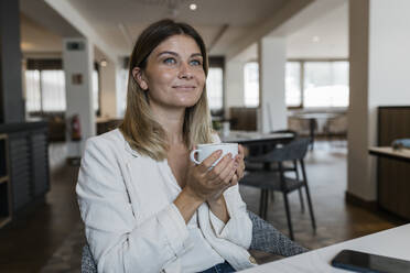 Smiling businesswoman holding coffee cup at restaurant - JRVF03109