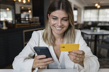 Glückliche Geschäftsfrau mit Kreditkarte beim Online-Einkauf per Smartphone im Restaurant - JRVF03118