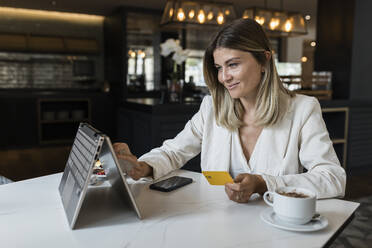 Smiling businesswoman holding credit card doing online shopping through laptop at restaurant - JRVF03120