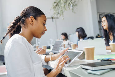 Businesswoman working on tablet PC at desk in coworking space - MEUF06629