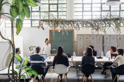 Geschäftsfrau erklärt Kollegen im Coworking Space die Windkraftanlage - MEUF06638