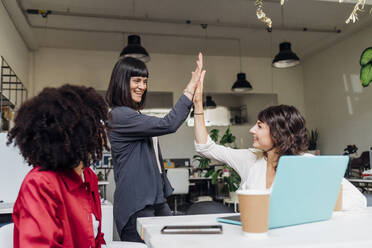 Smiling businesswomen giving high-five in coworking office - MEUF06650