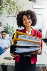 Smiling businesswoman holding files at office - MEUF06660