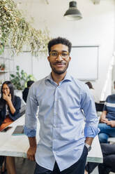 Smiling businessman with colleagues in background at workplace - MEUF06667