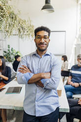 Confident businessman with arms crossed at desk in office - MEUF06668