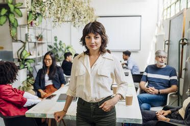 Confident businesswoman with colleagues in background at workplace - MEUF06670