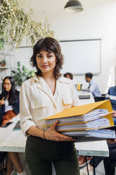 Confident businesswoman holding files at coworking office - MEUF06672