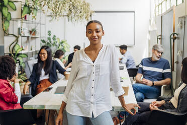 Smiling young businesswoman by multiracial colleagues at desk in office - MEUF06676