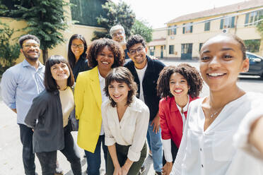 Lächelnde Geschäftsleute und Geschäftsfrauen machen ein Selfie an einem sonnigen Tag - MEUF06693