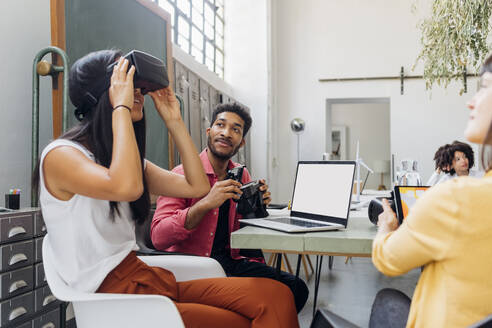 Businesswoman watching VR goggles by colleague at workplace - MEUF06723