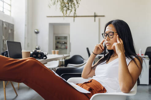 Businesswoman with documents having headache at workplace - MEUF06736