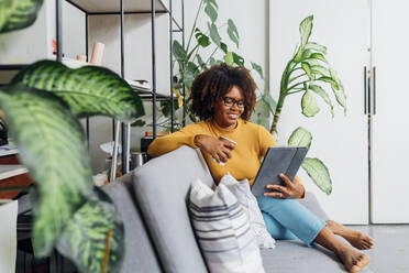 Smiling businesswoman using tablet PC on sofa at office - MEUF06740