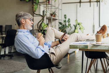 Businessman with eyeglasses using smart phone at desk in office - MEUF06744