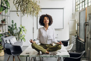 Young businesswoman meditating on desk at office - MEUF06752