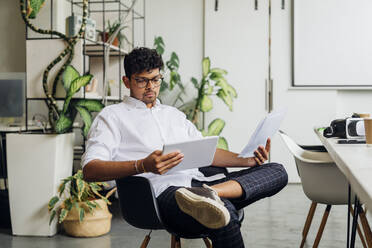 Businessman with documents using tablet PC on chair at workplace - MEUF06757