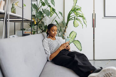 Young businesswoman using smart phone on sofa at office - MEUF06760