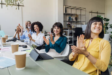 Smiling businessmen and businesswoman clapping hands at desk in office - MEUF06770