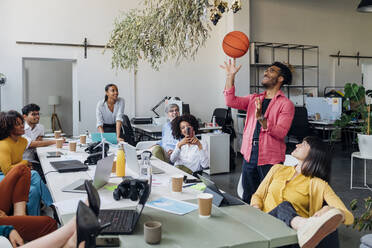 Businessman spinning basketball by colleagues in office - MEUF06771